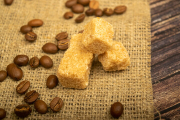Coffee beans and pieces of brown sugar cane homespun fabric with a rough texture. Close up.