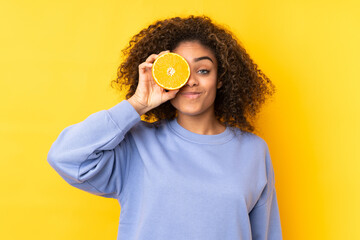 Young African American woman holding an orange over yellow background