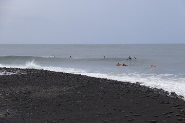 Plage de sable noir et surfeurs à Tahiti, Polynésie française	