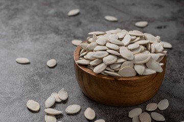 Pumpkin seeds in wooden bowl on the cement floor. Healthy eating and diet snack concept.