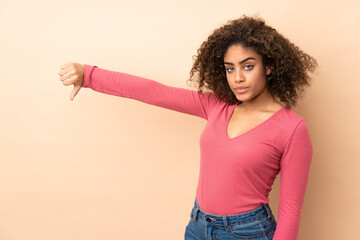 Young African American woman isolated on beige background showing thumb down with negative expression