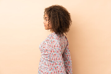 Young African American woman isolated on beige background in back position and looking back