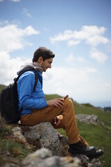 A young male tourist sitting on a rock. He is on the summit of Stara Planina (Balkan Mountains) and enjoying the view. In one of his hands, he's holding a wooden flute/ pipe.