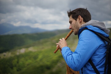 A side view of a young male tourist playing a wooden reed-pipe/ flute. He is on the summit of Stara Planina (Balkan Mountains). 
