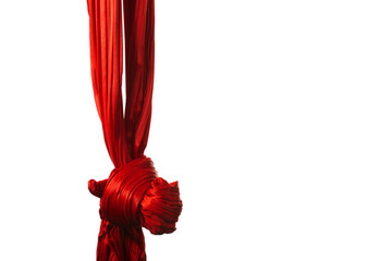 Red aerial ribbon tied in knot for aerial acrobatics and gymnastics hanging on white background....