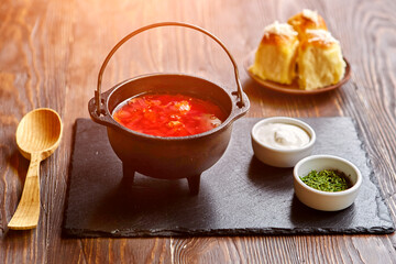 Traditional Ukrainian Russian vegetable borscht on an old wooden background in portioned cast iron. With herbs, sour cream and garlic bread.