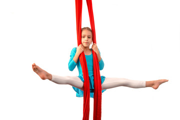 Little acrobat girl doing splits in the air holding on to a red air ribbon on a white background. Acrobatics concept. Advertising space