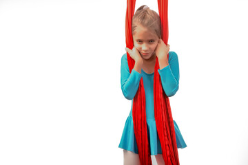 Concentrated little caucasian girl in a blue suit does gymnastic exercises on a red aerial ribbon