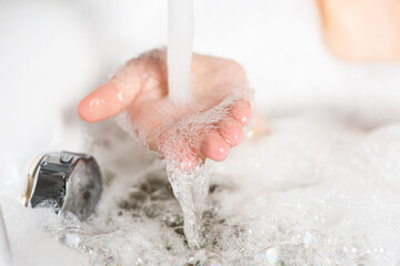 Fototapeta premium Close up female hand in soapy foam was substituted under the stream of water in the sink. Concept of cleanliness and hygiene during the coronovirus pandemic