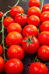 two ripe branch of cherry tomatoes in drops of Ross water on a black embossed table. copy space, close up, vertical orientation