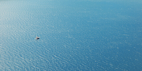 A yacht or a boat floats alone on the big water in sun glare. Open sea without wind.