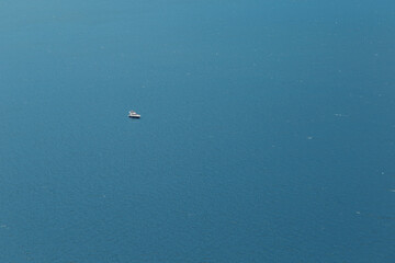 Fototapeta na wymiar A yacht or a boat floats alone on the big water in sun glare. Open sea without wind.