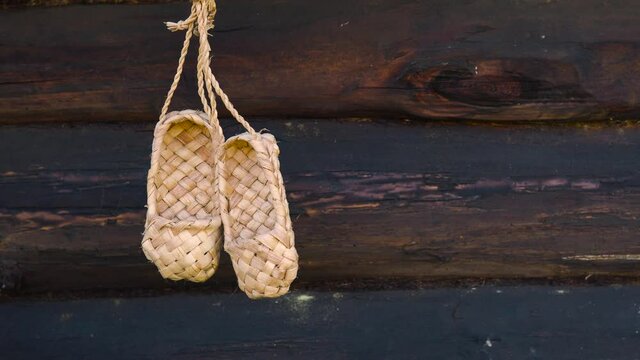 Antique handmade rustic shoes - bast shoes. A pair of bast shoes hanging on the background of a wooden log wall.