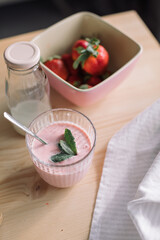 Healthy dessert with mint, fresh strawberries, glass bottle of milk on kitchen counter.