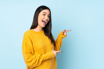 Young caucasian woman isolated on blue background surprised and pointing side