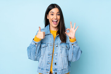 Young caucasian woman isolated on blue background showing ok sign and thumb up gesture