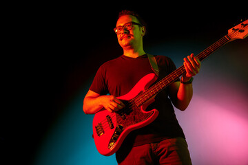 Obraz premium Young caucasian inspired and expressive musician, guitarist performing on gradient colored background in neon light. Concept of music, hobby, festival, art. Joyful artist, colorful, bright portrait.