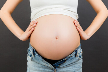 Close up of naked pregnant woman's belly wearing opened jeans at colorful background with copy space. Pregnancy concept