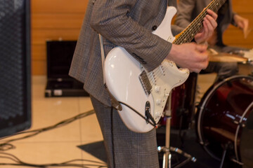 Fototapeta premium Guitarist plays solo. Grey suit and white guitar. There's a drum kit in the background.