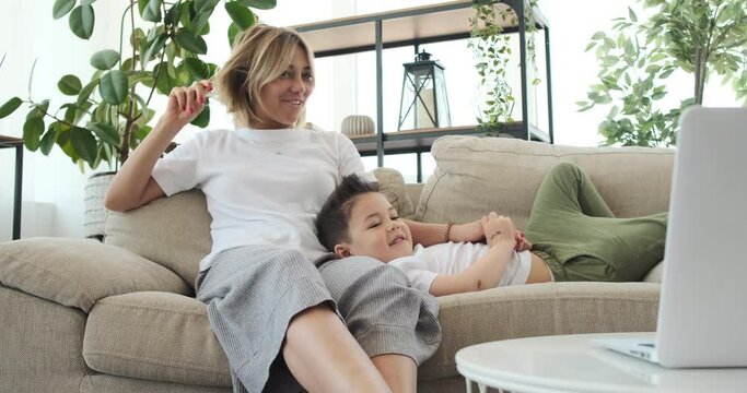 Mother and son watching movie on laptop relaxing on sofa at home