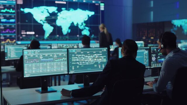 Team of Professional Computer Data Science Engineers Work on Desktops with Screens Showing Charts, Graphs, Infographics, Technical Neural Data and Statistics. Low Key Control and Monitoring Room.