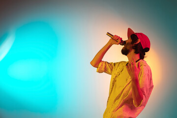 Motion. Young inspired and expressive musician, singer performing on gradient colored background in neon light. Concept of music, hobby, festival, art. Joyful artist, colorful, bright portrait.