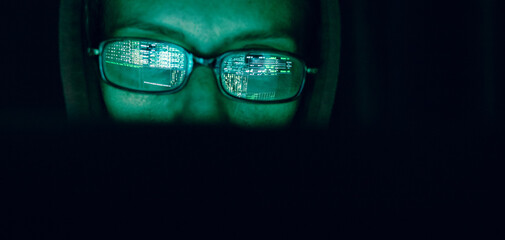 hacker at computer data reflecting in eyeglasses