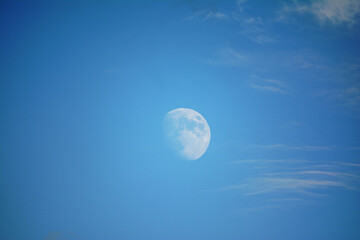 Moon in the daytime, blue sky with small clouds