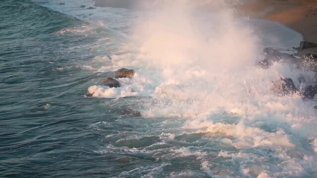 Wave approaching on the rocks and exploding hard on them at spanish coast during daytime.