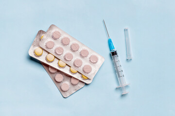 Medical syringe with medicine pills on blue background. Injectable drugs, vaccination concept.
