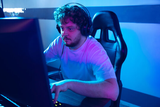 Cyber sport. Fully concentrated professional cybersport gamer playing important match. Caucasian male model practicing, training before tournament alone in neon light. E-sport, gamer, streamer.