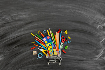 Shopping cart with school supplies on blackboard background. Back to school concept. © mallmo