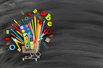 Back to school concept. School supplies in shopping cart on blackboard background. 