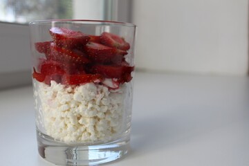 preparing Breakfast snacks healthy food in a glass cottage cheese and fruit berries red strawberries cut into pieces side view on a white background there is a place to insert text