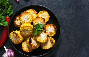 Baked hot corn with butter in a cast-iron pan on a black background. View from above.