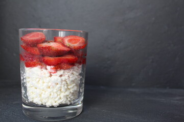 preparing Breakfast healthy snack lunch dinner food in a glass cottage cheese and berries fruit with strawberry slices on a gray stone black background with space for text