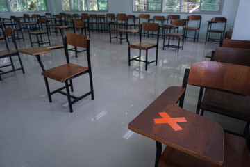 X mark on the wood lecture chairs place distancing in the empty classroom. Concept during the Coronavirus disease COVID-19 outbreak and pandemic in the 2020s. Back to school concept.
