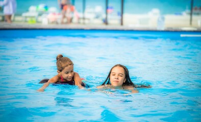 Two little sisters girls are swimming in a large pool with clear blue water of mine near the hotel on the background of the sea and the beach. Concept vacation tropical hot country with children