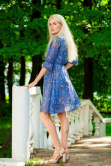 Obraz na płótnie Canvas Portrait of a young blonde woman in blue dress walking in summer parkpark
