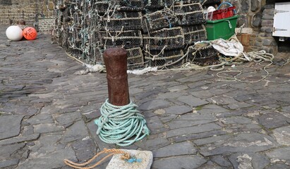 A closeup of a rusty, brown bollard with coiled rope on the quayside in a fishing harbour in England.