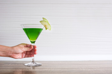 Female hand with green appletini cocktail on wooden table.Copy space