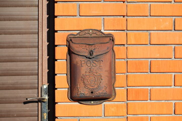 rusty old mailbox on a fence wall made of red textured brick surface