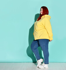 Side view of a flirtatious curvy young woman putting one foot on toe in front of other. Full length shot isolated on blue