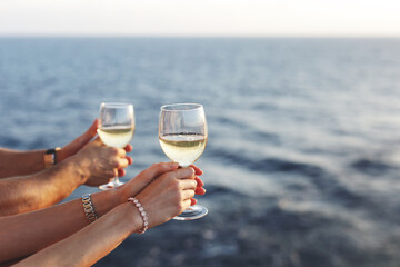 male and female hand hold glasses with white wine on a cruise liner against the sunset