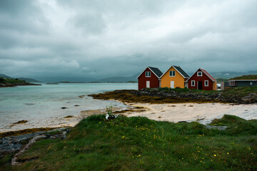 Fototapeta na wymiar Scandinavian colorful yellow and red wooden huts. Summer houses (cabin) on the azure sea, beautiful sandy light beach in the Sommaroy island, northern Norway. Horizontal orientation.
