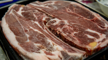 Close up detail view of raw beef lamb meat steak in a black tray packaging at the kitchen. Selective focus on foregrounds.