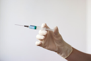 A rubber gloved hand holds a syringe with a needle filled with a blue liquid