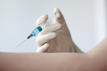 A rubber gloved hand holds a syringe filled with a blue liquid and gives an injection to the other hand