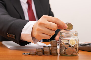 Businessman putting coins in glass, holding pen to record, concept saving money