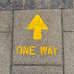 Bright yellow one way arrow sign spray painted onto street to direct pedestrians which way to walk around the town centre during Corona Virus pandemic in the United Kingdom